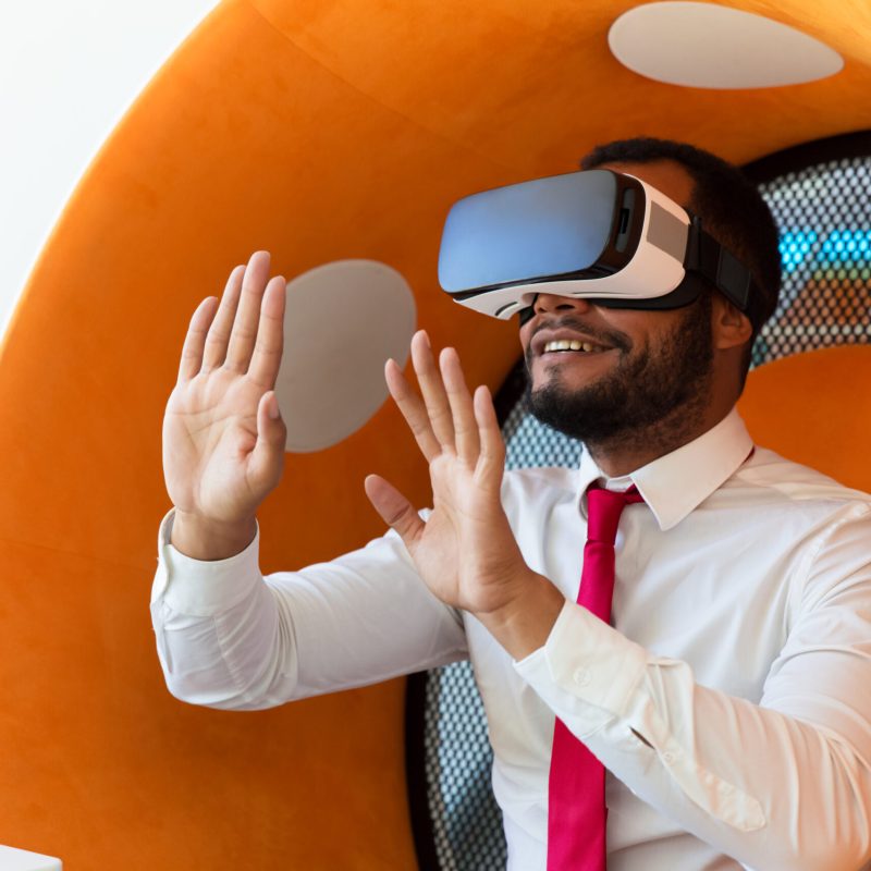 Happy businessman excited with VR experience. Man wearing virtual reality headset, sitting in interactive chair and touching air. Visual technology concept
